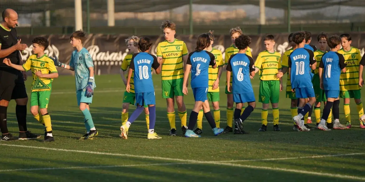 A group of young boys in green and yellow uniforms standing together and shaking hands on a sports field during the Mina Cup 2024.