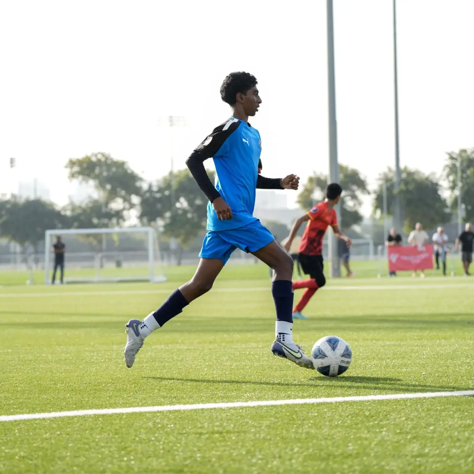 A player in blue kicking a soccer ball on a DOFA Season grass field.