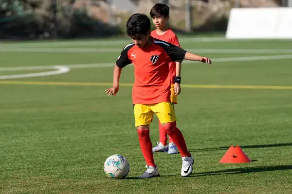 Young Boy in Red Shirt Participating in Football Coaching in Dubai