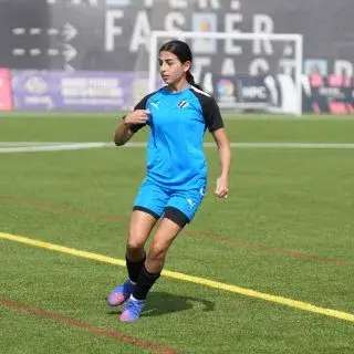 Young female soccer player in uniform kicking a soccer ball on the field.