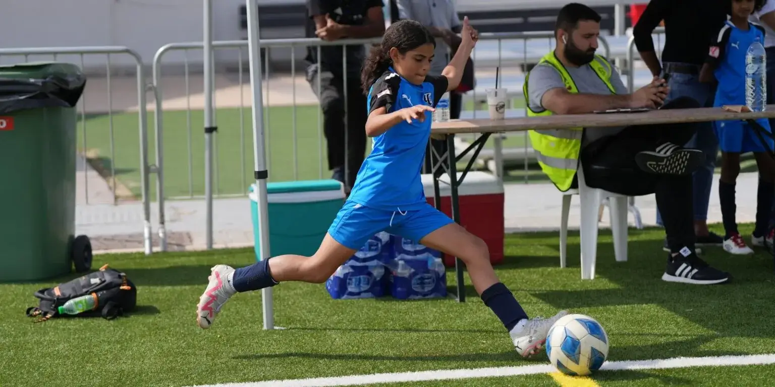 DOFA Season 2023 | A young girl playing soccer on a field, kicking a ball with determination.