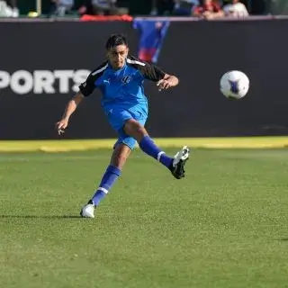 Athlete in blue kicking football ball on green field.