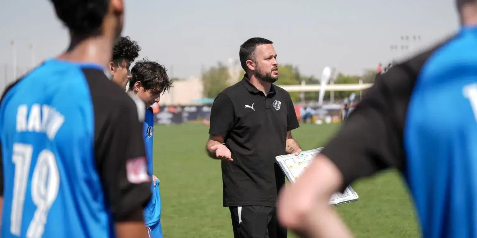 Coach strategizing with players on the field during a Mina cup football match.