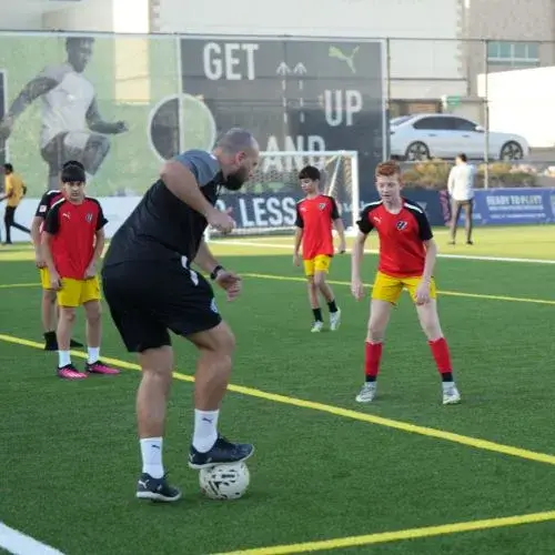 La Liga Academy Dubai Fees | A coach enjoying a game of soccer with kids outdoors.