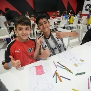 Summer Camp In Dubai | Two boys are smiling and giving thumbs up while sitting at a table with coloring sheets and crayons.