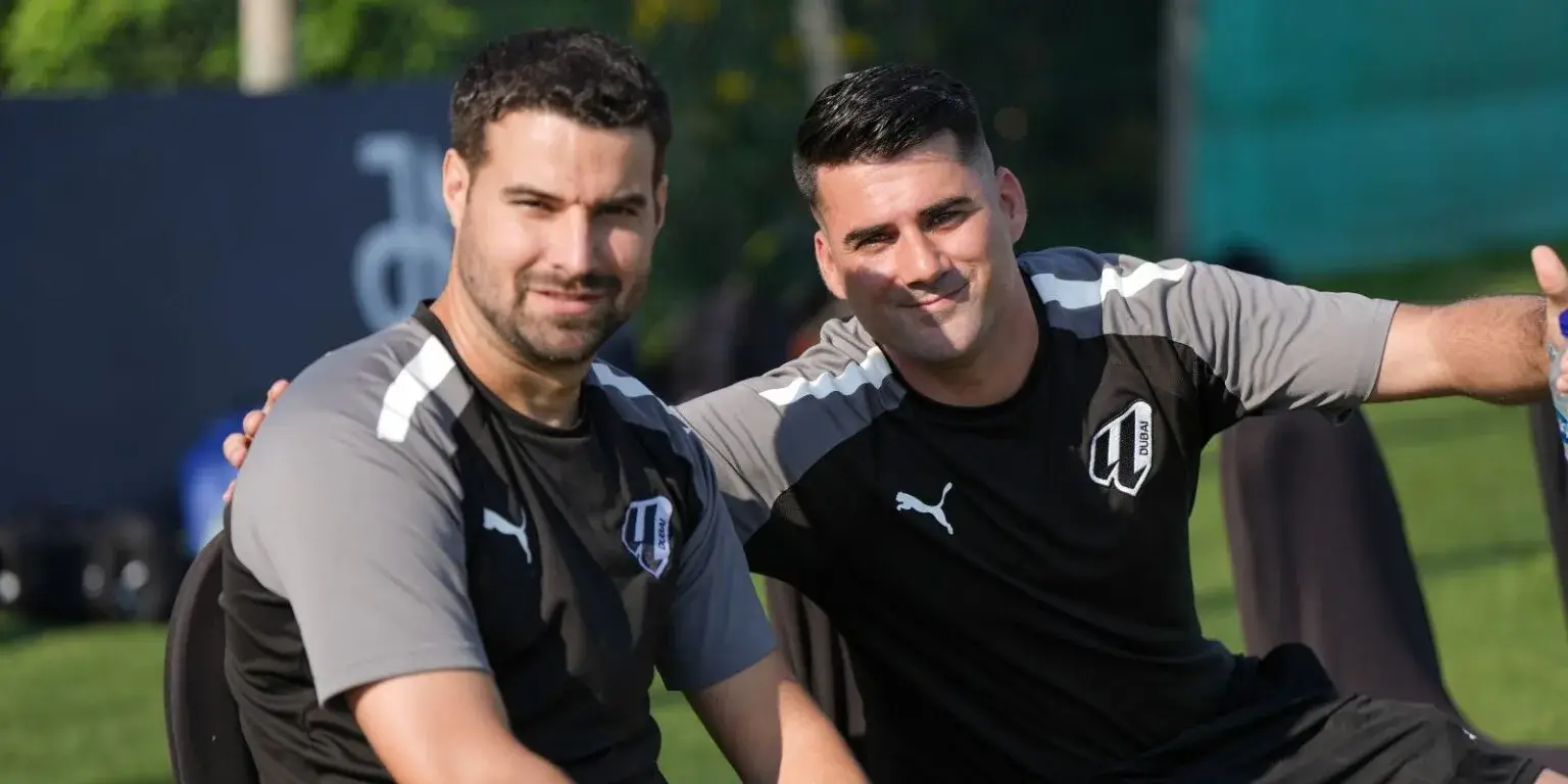 Two soccer players taking a rest on the field, having a conversation during a game break.